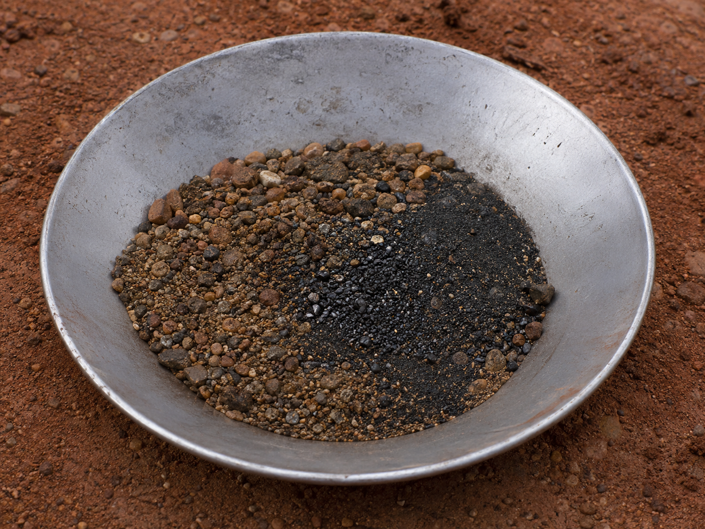 Cassiterite-bearing gravel in a geological sample pan